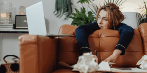 אישה נשענת על הספה מסתכלת על הלפטופ מתקשה לעשות מה שהיא יודעת שהיא צריכה