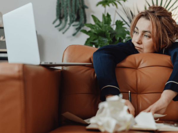 אישה נשענת על הספה מסתכלת על הלפטופ מתקשה לעשות מה שהיא יודעת שהיא צריכה